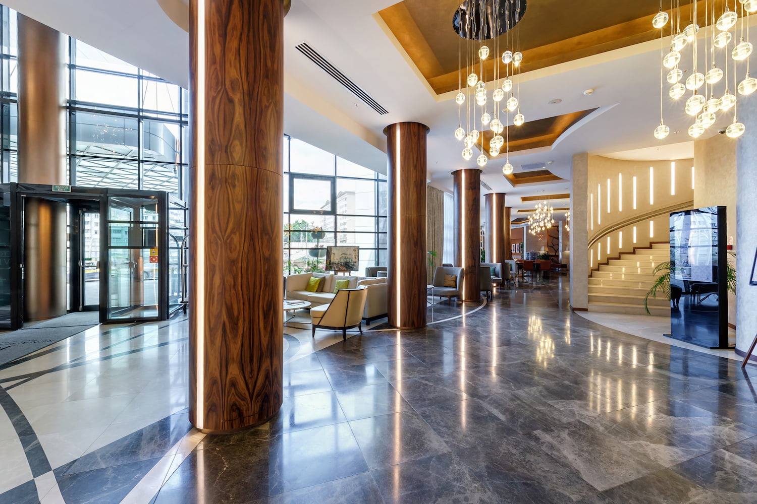 Salão de hotel com colunas, lustres, porta giratória e arquitetura de luxo.